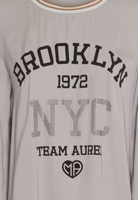 Light gray shirt with black printed text "BROOKLYN 1972 NYC TEAM AUREL," textured elements on "NYC," and a heart logo at the bottom.
