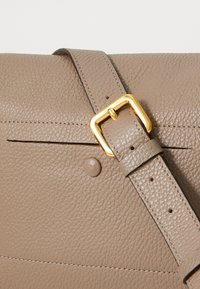 Sac à main en cuir taupe avec une surface texturée, quincaillerie en ton or, et une large sangle réglable avec un détail à pression.