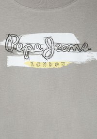 Grå bomulds T-shirt med et håndtegnet logo i sort med gule accenter og en hvid penselstræk baggrund. Rund halsudskæring, korte ærmer.