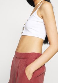 Débardeur blanc court à texture côtelée avec des boutons sur le devant, associé à un pantalon ample taille haute de couleur rouille avec des poches.