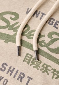 Felpa con cappuccio beige caratterizzata da grafiche testuali verdi e blu. Tessuto misto cotone con lacci piatti e punte in metallo argentato.