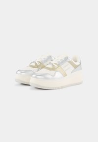Metaliczne srebrne i białe sneakersy z grubą podeszwą, z gładkimi teksturami i warstwowymi wzorami, akcentowane jasnobeżowymi paskami.