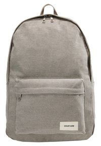 Sac à dos en toile grise avec un dessus arrondi, une fermeture éclair, une poche avant et une étiquette de marque. Comprend deux bretelles pour le porter.