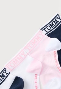 Δύο ζευγάρια κάλτσες αστραγάλου, ένα λευκό με σκούρο μπλε φτέρνα και περιλαίμιο, ένα ροζ και λευκό, και τα δύο με το λογότυπο "Tommy Hilfiger" στο περιλαίμιο και στη σόλα.