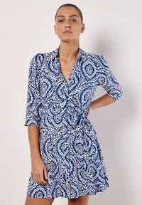 Abito camicia blu e bianco con motivo, colletto, maniche a tre quarti e vita legata, realizzato in un tessuto leggero e con gonna svasata.