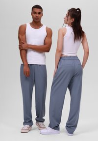 Pantalons à rayures grises avec taille élastique, portés avec des débardeurs blancs et des baskets décontractées. Le modèle prend des poses de face et de dos.