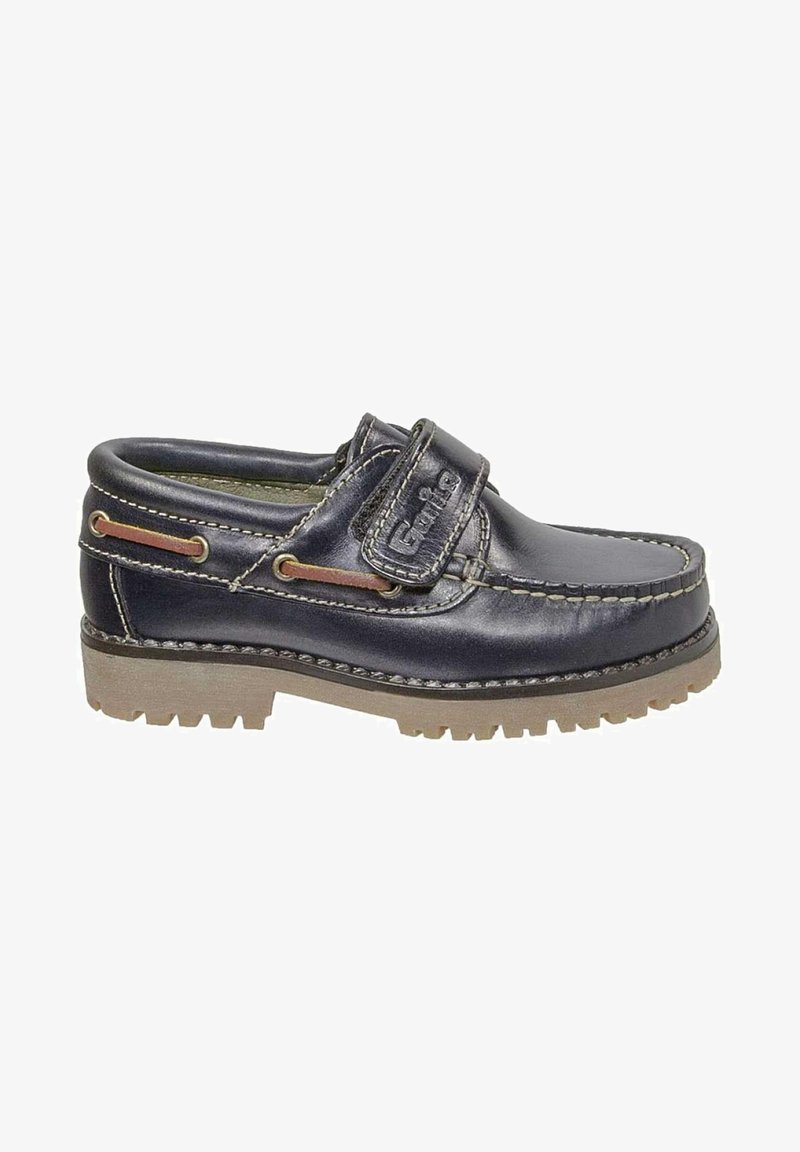 Zapato slip-on de cuero azul marino con una correa de velcro, suela de goma con ranuras de tracción, y costuras y acentos en contraste en color marrón claro.