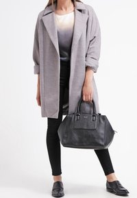 Abrigo gris de gran tamaño con mangas enrolladas, combinado con un bolso de cuero negro y pantalones negros ajustados. La modelo lleva zapatos planos negros.