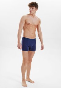 Námorně modré boxerky vyrobené z měkkého materiálu, s přiléhavým střihem a elastickým pasem s decentním logem, nošeny modelem.