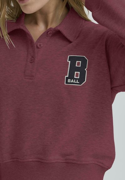 Bordó pulóver, galléros nyakkal, két gombbal és fekete-fehér hímzett "B BALL" mintával a mellkason.
