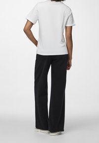 Vit t-shirt med kort ärm och rund halsringning, kombinerad med högmidjade svarta vida byxor, som visar en avslappnad passform och enkel design.