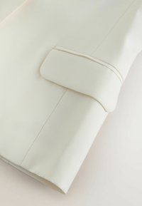 Close-up of a cream-colored long sleeve shirt cuff with a neat seam and folded edge detail.