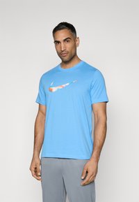 Camiseta Nike de color azul claro, hecha de algodón, con un diseño de logo multicolor en el pecho. Cuello redondo y mangas cortas.