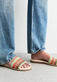 Las sandalias deslizantes tejidas multicolores cuentan con un borde trenzado, suela plana y plantilla suave, combinadas con unos jeans de pierna recta en azul claro.