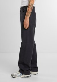 Pantalones de algodón gris oscuro con corte recto, bolsillos laterales y diseño de tiro bajo; combinados con zapatillas deportivas blancas y grises.