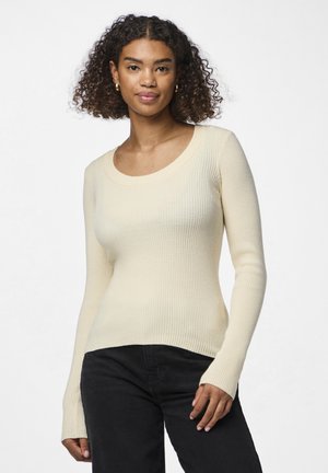 Geribbeld, lang mouwen top in lichtbeige met een ronde hals; getailleerde pasvorm; textiel stof; gecombineerd met zwarte broek.