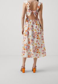 Robe midi fleurie avec des bretelles volantées, dotée d'une découpe au dos et d'une taille élastique. Motifs de fleurs colorées sur un fond clair.