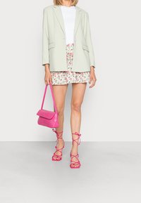 Ljusgrön blazer över en vit topp, blommig minikjol, handväska i rosa krokodilprägling och rosa sandaler med remmar och platåklackar.