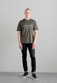 Tume oliivroheline puuvillane T-särk, millel on trükk "Emporio Armani Milano 1981", kombineeritud mustade teksade ja mustade madalate tossudega.