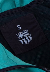 Groene en zwarte jas interieur met een maatlabel met "S" en het Barcelona FC-logo in het wit. Geweven stof met gaasaccenten.