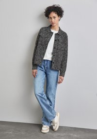 Svart och vit tweedjacka med krage, i kombination med en vit ribbad topp, ljusblå denimjeans och beige och vita sneakers.