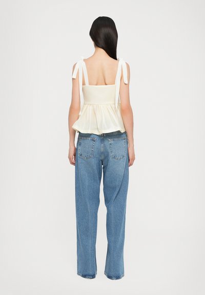 Top peplum crema con tirantes regulables de cintas, combinado con vaqueros de talle alto azul. Tela suave con un corsé texturizado y un dobladillo acampanado.