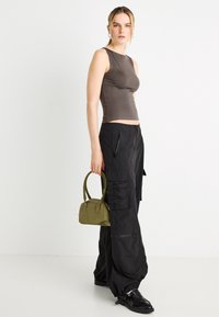 Débardeur marron moulant, pantalon cargo noir avec poches, et petit sac à main vert. Le mannequin se tient devant un fond blanc, portant des chaussures noires.