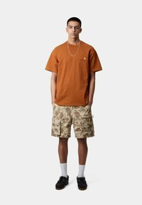 T-shirt in cotone arancione con scollo rotondo e maniche corte, abbinato a pantaloni cargo mimetici con multiple tasche e un dettaglio con bottone.