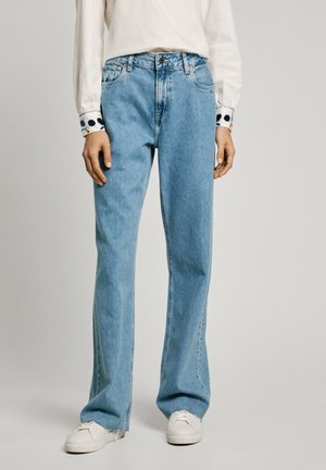 Lyseblå denim jeans med lige ben, høj talje og fem-lomme-design; parret med en hvid bluse med lange ærmer og mønstrede manchetter.