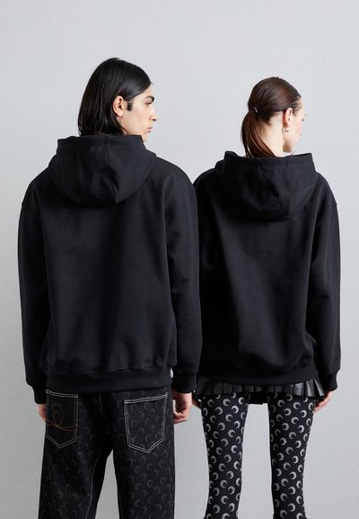 Hanorace cu glugă negre, realizate dintr-un amestec de bumbac, având o croială lejeră. Spatele nu are branding vizibil. Poartă cu pantaloni negri cu model.
