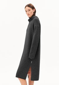 Robe en laine grise surdimensionnée avec un col haut, des fentes latérales et de longues manches, mettant en avant une texture douce et des lignes épurées.