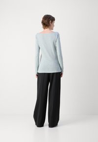 Šviesiai mėlynas ilgomis rankovėmis viršus su laivagaliu, derinamas su plačiais juodais kelniais. Minkšta, tekstūruota medžiaga su laisvu siluetu.