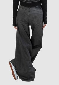 Szerokie szare jeansy z denimu o gładkiej fakturze, z tylnymi kieszeniami i subtelną metką marki na pasku, w połączeniu z czarną bluzką.