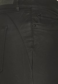 Pantalones vaqueros de denim negro con un corte ajustado, que presentan bolsillos traseros, costuras en tono y una textura suave. Marca sutil en la cinturilla.