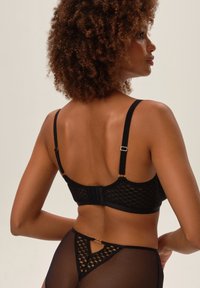 Czarny koronkowy biustonosz z geometrycznym wzorem, regulowanymi ramiączkami i zapięciem na haftkę z tyłu. Przezroczyste czarne majtki z detalami akcentującymi.