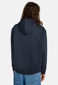 Felpa oversize blu navy realizzata in tessuto morbido, dotata di cappuccio con lacci, polsini e orlo a coste. Dettagli della cucitura ben visibili.