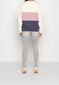 Sudadera en bloques de color blanco roto, rosa y azul marino; material de algodón con puños y dobladillo acanalados. Vaqueros ajustados grises y zapatillas casuales.