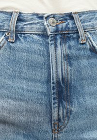 Jeans de mezclilla azul con costuras naranjas, que presentan un cierre frontal con botón, cinturillas y una textura ligeramente desgastada.