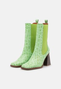 Botines verdes con textura de efecto cocodrilo estampada. Presentan un tacón cuadrado alto y paneles elásticos laterales para facilitar su uso.
