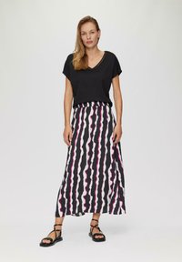 Zwarte v-hals t-shirt gecombineerd met een lange rok met verticale zwart, wit en roze golvende strepen; zwarte sandalen met bandjes maken de look compleet.