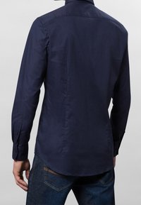 Mörkblå långärmad skjorta med klassisk krage, slät textur, knäppta manschetter och en rundad nederkant. Används tillsammans med mörka jeans.