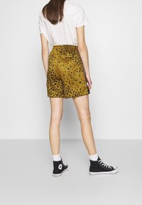 Pantaloni corti giallo a stampa leopardata con vestibilità rilassata e vita elasticizzata, abbinati a scarpe nere alte e calzini bianchi alla caviglia.