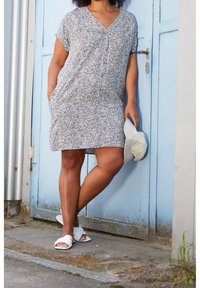 Robe courte à motif noir et blanc avec un col en V, des manches courtes et deux poches latérales. Portée avec des sandales blanches et un chapeau beige.