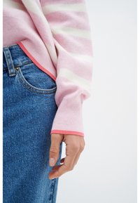 Pull en rayures roses avec des poignets côtelés et une accent rose, associé à un denim bleu, mettant en avant une coupe décontractée et confortable.