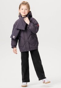 Grå polstret jakke med hætte, diamantquiltet mønster, sidelommer og rød logoaccent. Kombineret med sorte jeans og hvide sko.
