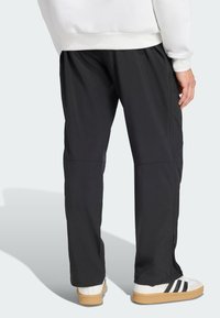 Svarta träningsbyxor med lös passform, avsmalnande ben, sidoreningar och en mjuk textur, kombinerade med vita sneakers med svarta ränder.