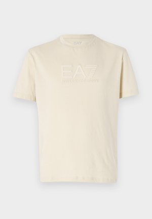 T-shirt color crema realizzato in morbido cotone, con un logo EA7 in rilievo sulla parte anteriore e un classico colletto a girocollo. Maniche corte.