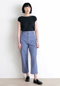 Top preto de manga curta combinado com jeans de cintura alta em azul claro. Os jeans têm corte reto; conjunto complementado por sapatos pretos brilhantes.