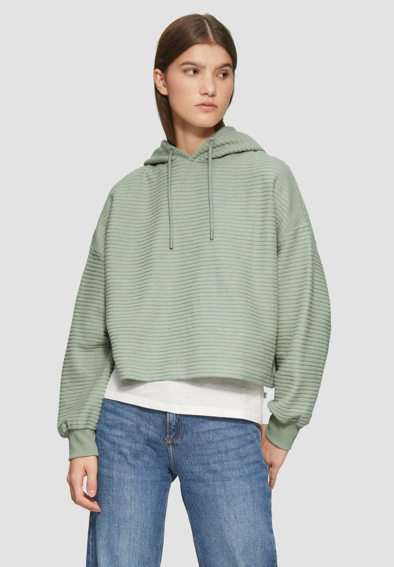 Hellgrüner, verkürzter Hoodie mit strukturiertem Rippdesign, Kapuze mit Zugband und langen Ärmeln, über einem weißen Shirt getragen.