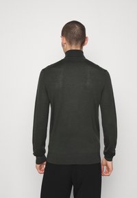 Tumma vihreä pusero, jossa on korkea kaulus, pehmeä materiaali, slim fit -muotoilu, pitkät hihat ja ribbatut yksityiskohdat hihoissa ja helmassa.